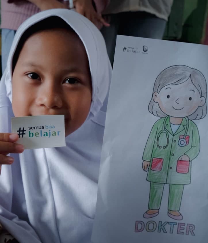 Seorang anak tersenyum di balik kartu #semuabisabelajar sambil memegang lembar mewarnai bertuliskan DOKTER — Tapak Asa — kelas inspirasi profesi · Ciamis, Jawa Barat